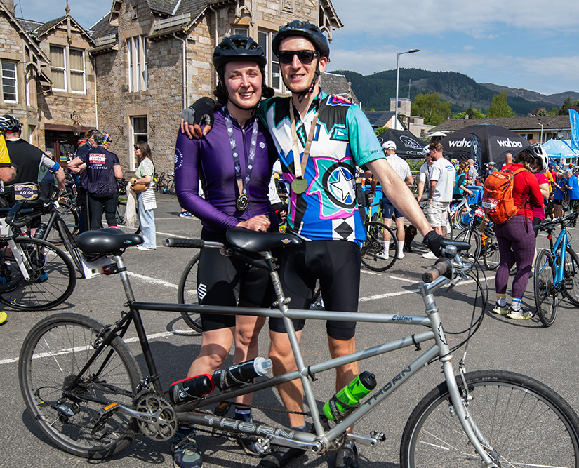 Two cyclists pose with their tandem bicycle after completing Etape Caledonia 2025 in Pitlochry, wearing finisher medals.